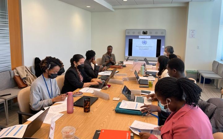 A group of fellows are seen sitting around a conference table, listening to Ms. Sonia Elliott, who is giving a brief overview of disarmament and the First Committee