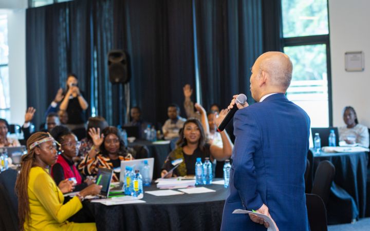 A man holding a mic facing African women and youth who are raising their hands