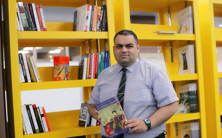 Sayf poses for a photo while holding a book at the Central Library