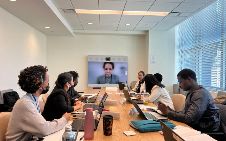 A group of fellows are seen sitting around a conference table, listening to Ms. Kim and Ms. Oosterwijk, who are discussing Information and Outreach