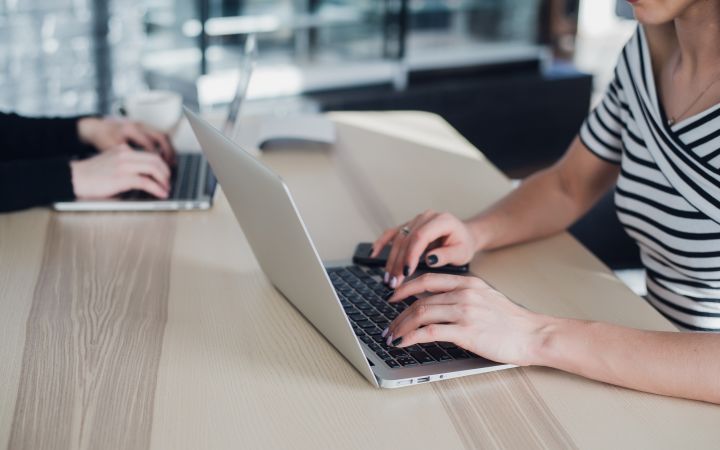 Close-up picture of the hands of two women typing on their laptops.