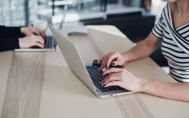 hands of two women across each other typing on their laptops placed on a table